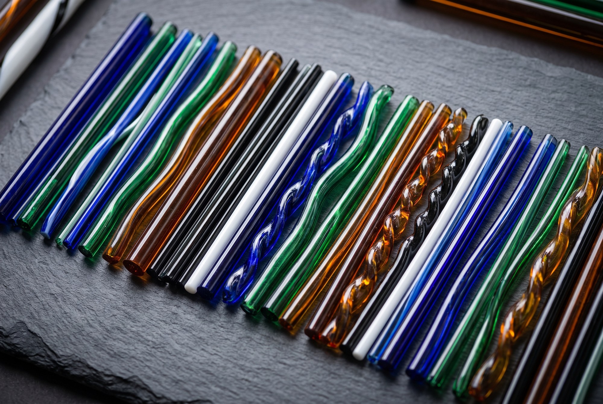Rows of pulled glass stringer and twisted cane in blue, green and amber laid out on slate