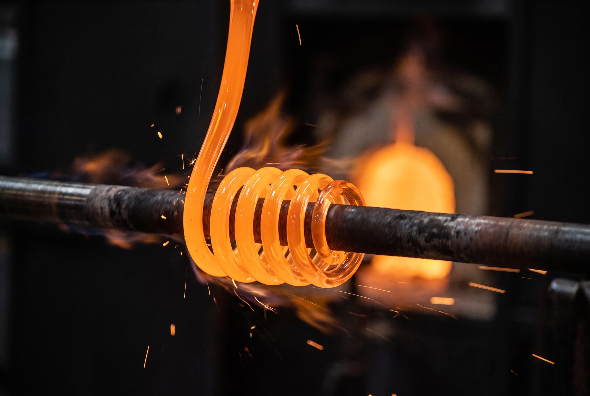 Molten glass wound into a glowing coil around a steel pipe as it leaves the kiln